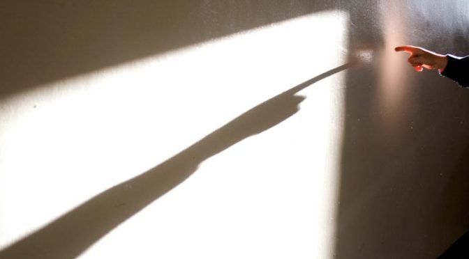 finger pointing to white wall with stark shadow
