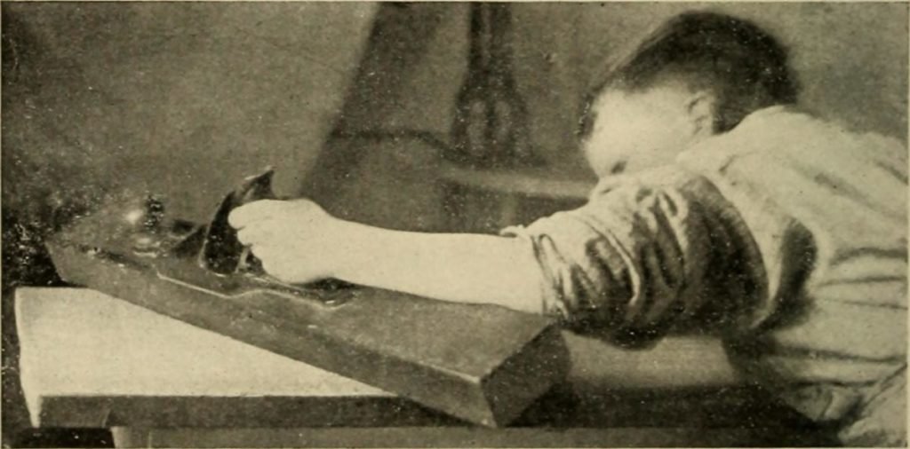 old 1900 photograph of a boy planing a piece of wood