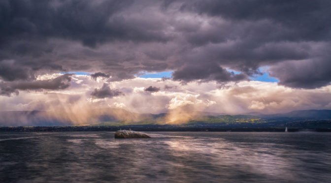 Photo of dark clouds with sun breaking through over water