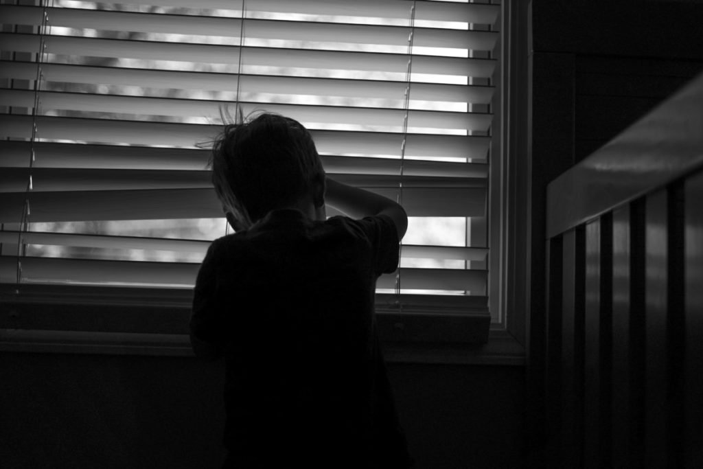 Photo of young boy peeking through blinds