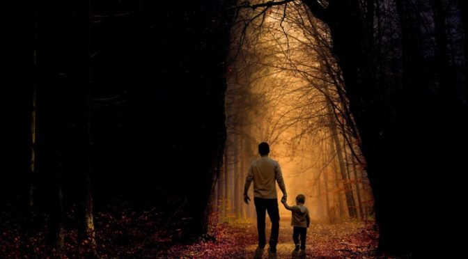 Father and son walking through an opening of light between trees