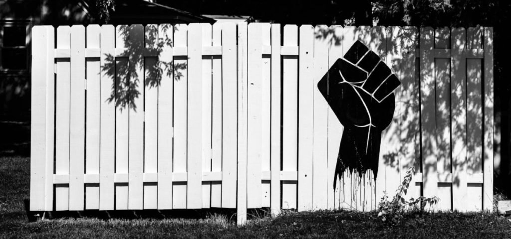 Black and white photo of black fist painted on white fence