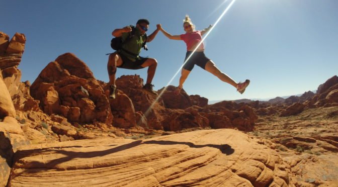 Two hikers jumping on large rock