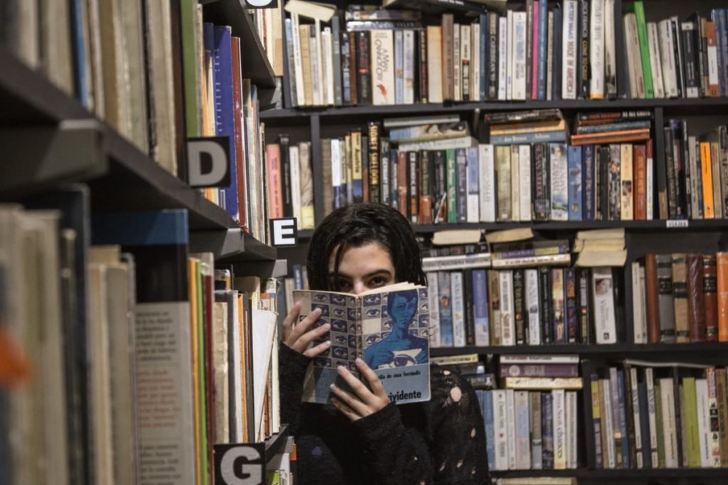 Photo of woman reading among shelves of bookstore