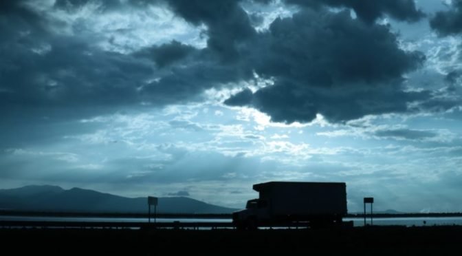 Silhouette of truck against cloudy, dark blue sky
