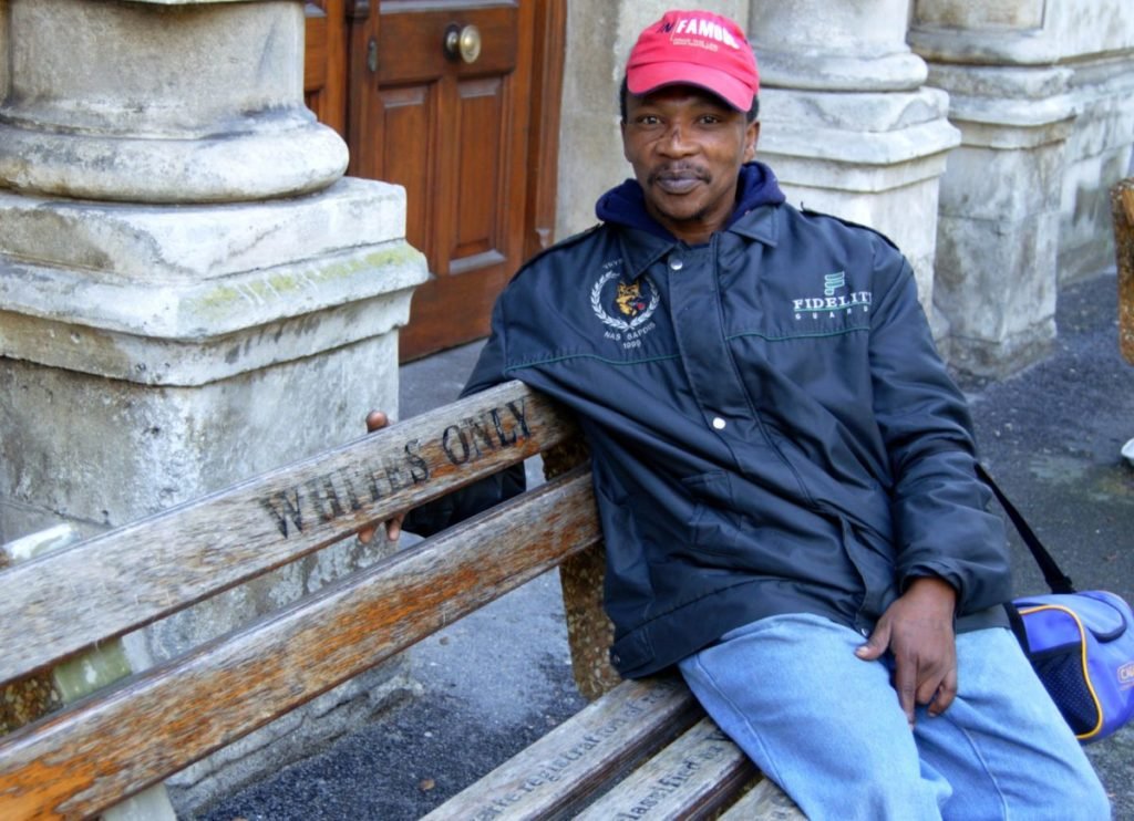 Photo of black man on bench that says "Whites Only"