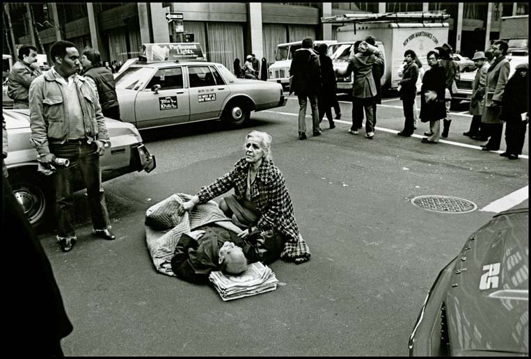 Black and white photo of man laying in road with woman kneeling by his side