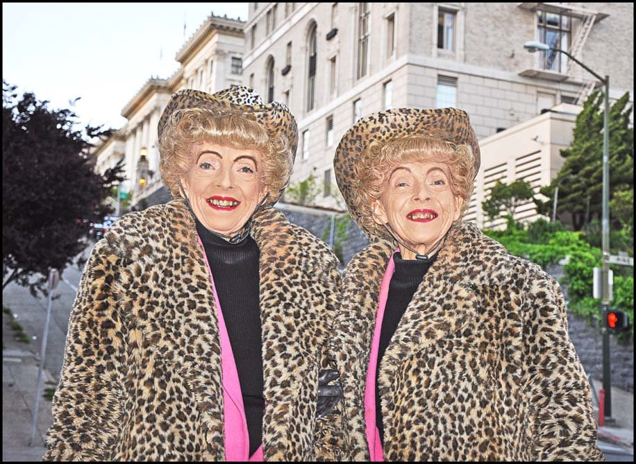 Color photo of elderly twin sisters in cheetah print coats and hats