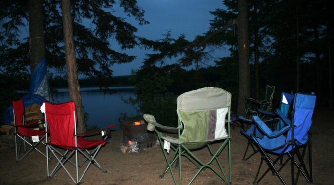Photo of empty camping chairs at lake at dusk