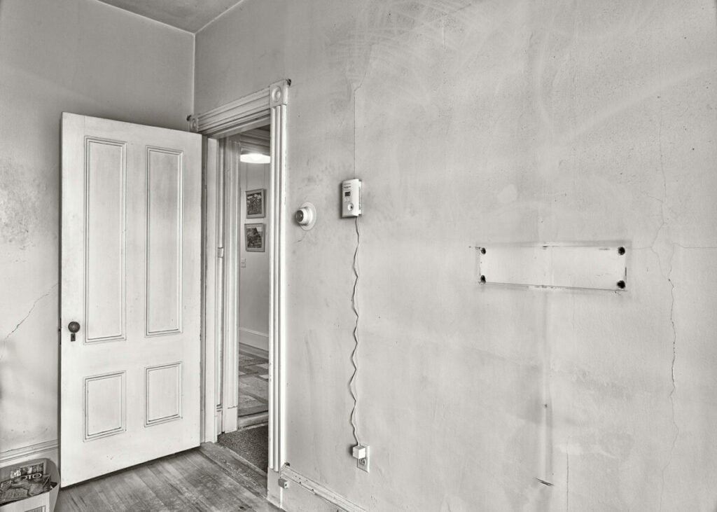 Black and white photo of empty room, with one thing plugged in wall