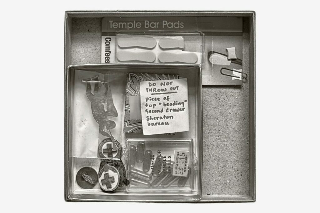 Black and white photo of box with odds and ends and a note that says "Do Not Throw Out"