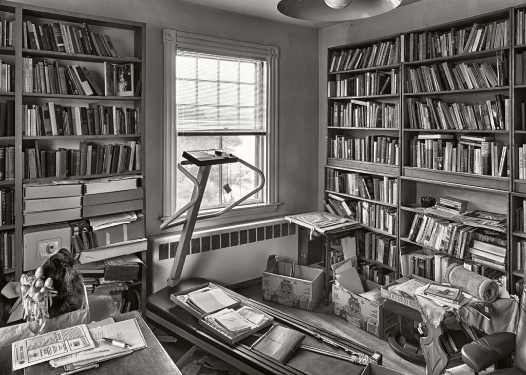 Black and white photo of study with books everywhere and a treadmill