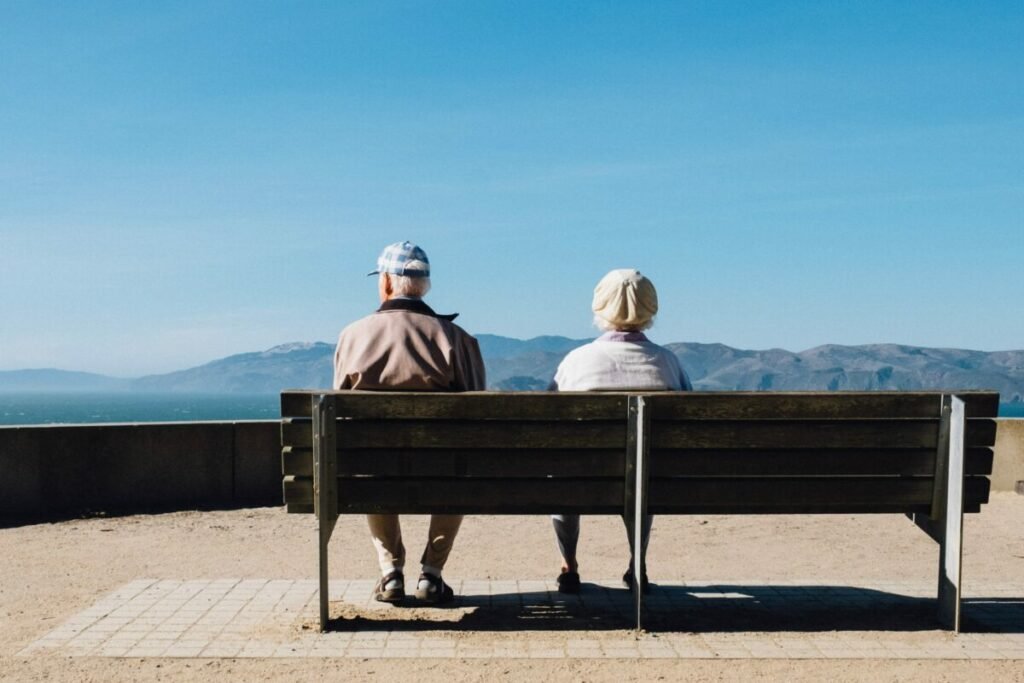 Photo from behind of older couple sitting on bench in front of mountains