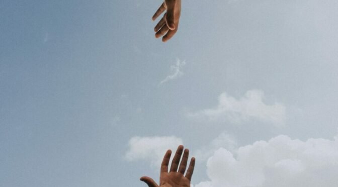 hand reaching up, another reaching down, blue sky background