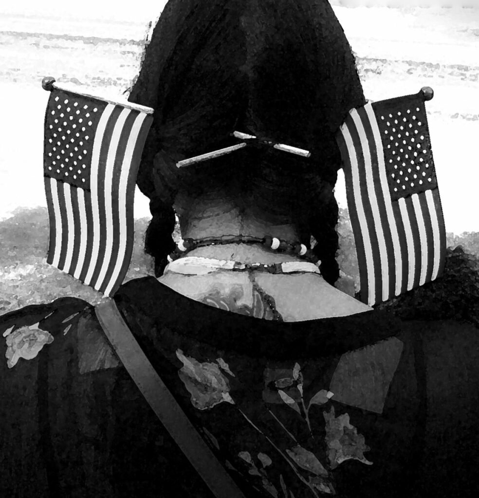 Black and white photo of woman from behind, with hair in braids and small American flags stuck through the braids
