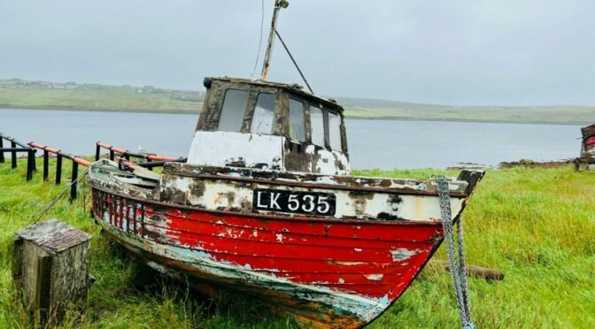 Photo of old red and white boat up on grass near water