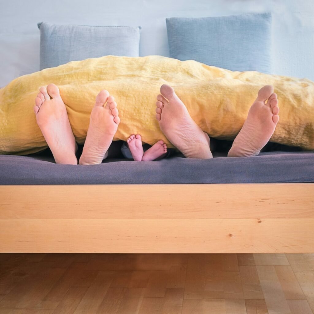 Photo of two sets of adult feet with one set of child's feet between, sticking out from end of covers