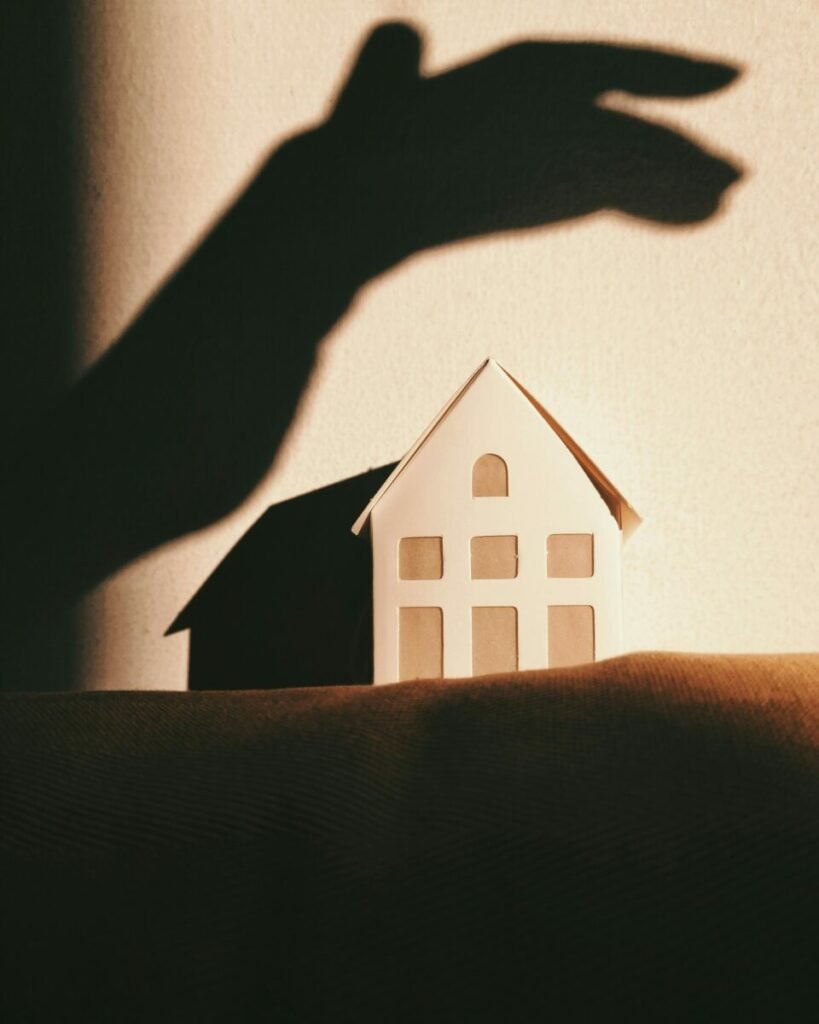 Photo of shadow of hand on wall above small house made of paper
