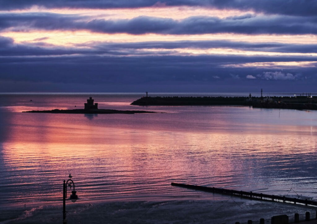 Photo of beach at dawn, with pink and purples in sky and reflecting off water