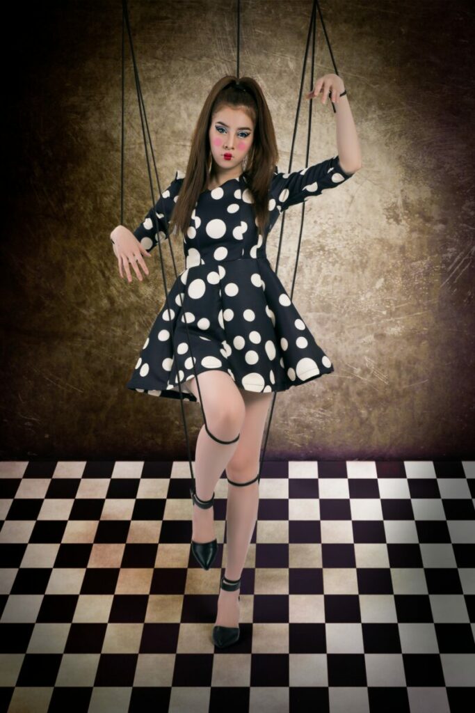 Photo of young woman dressed as marionette, with strings tied to arms and legs