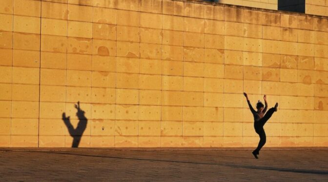 dancer and shadow cast on gold building at night