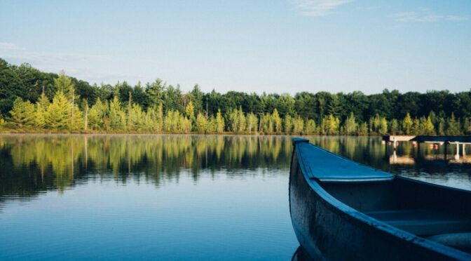 Photo of front of canoe on water, with forest in background