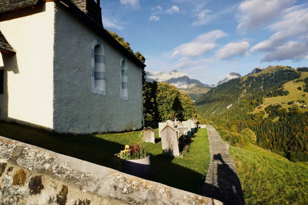 Photo of old white church, row of tombstones, surrounded by wall and rolling green hills