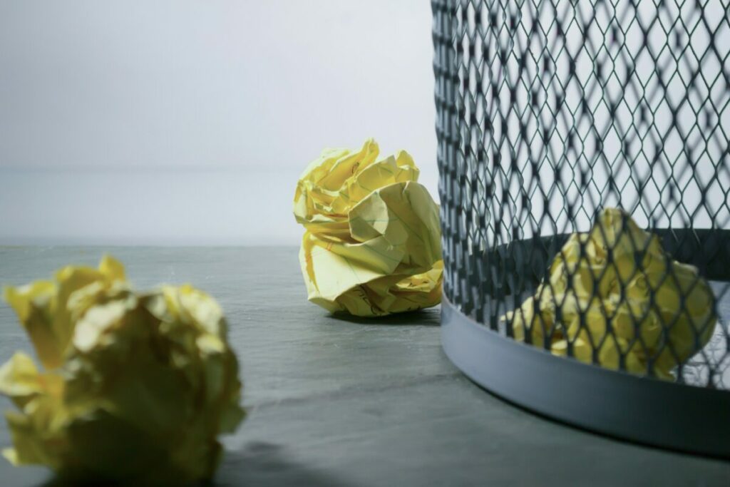 three crumpled pages of yellow paper and mesh trash can