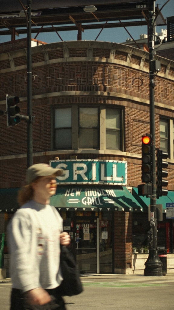 Photo of woman passing brick building with sign that says Grill on it
