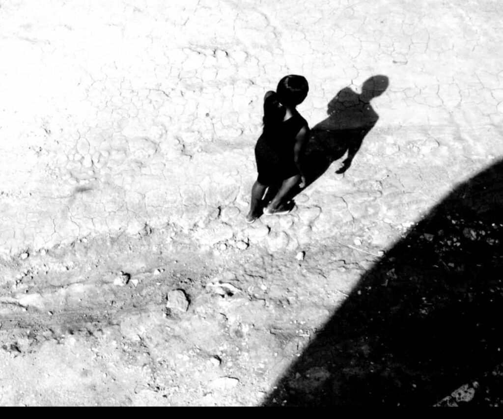 Black and white aerial photo of person walking along sand