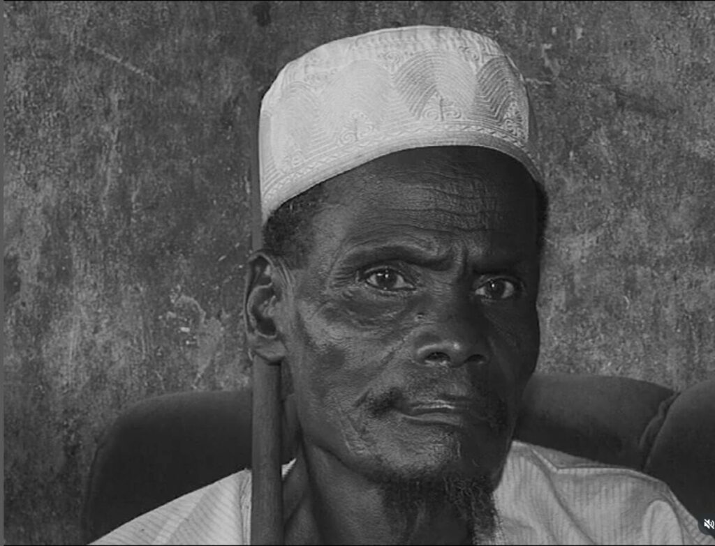 Black and white photo of black man with white hat against dark background