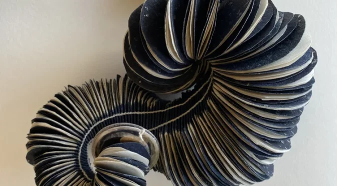Pages of books that are cut into circles twisted around itself on the wall