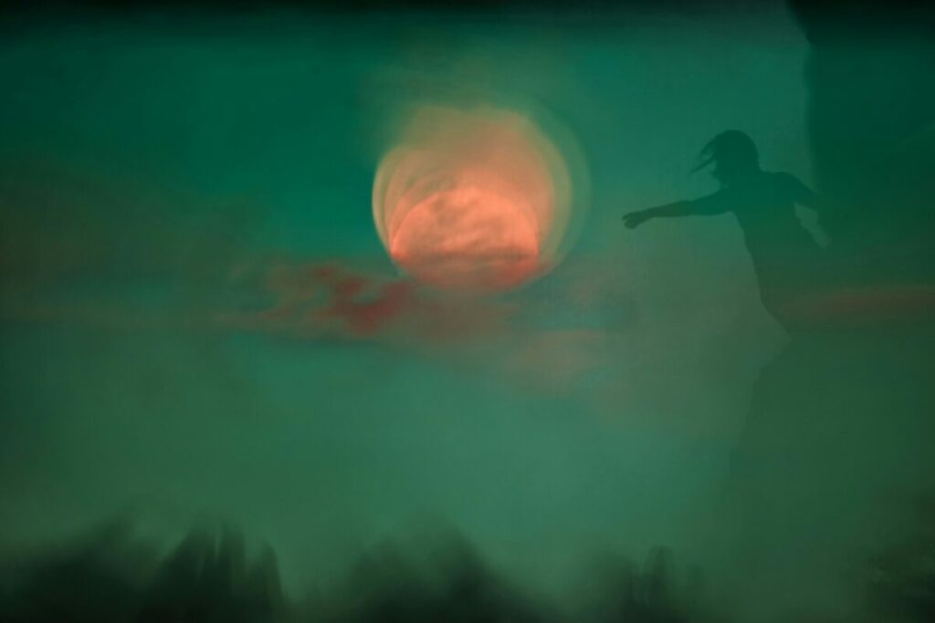 Abstract photo of person in silhouette reaching toward orange sun, all filtered with a green haze