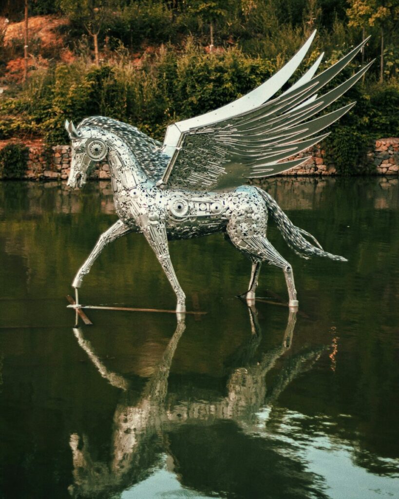 Photo of statue of winged unicorn in middle of lake and forest