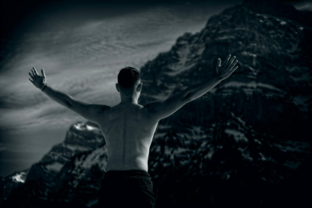 Posterior view of man stretching wide his arms in front of a mountain
