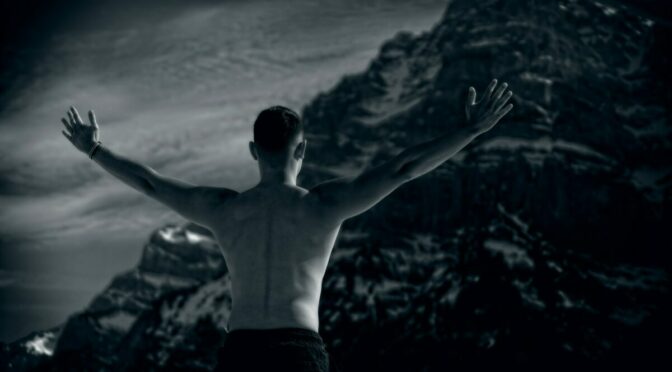 Posterior view of man stretching wide his arms in front of a mountain
