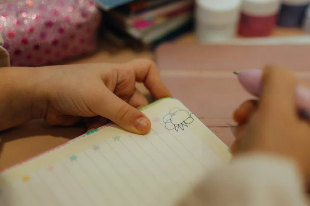 Photo of young girl's hands holding pen and open notebook with doodle inside