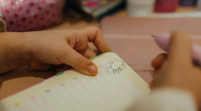 Photo of young girl's hands holding pen and open notebook with doodle inside