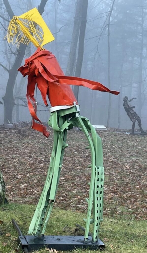 Sculpture of humanoid with yellow head, red shirt, green pants