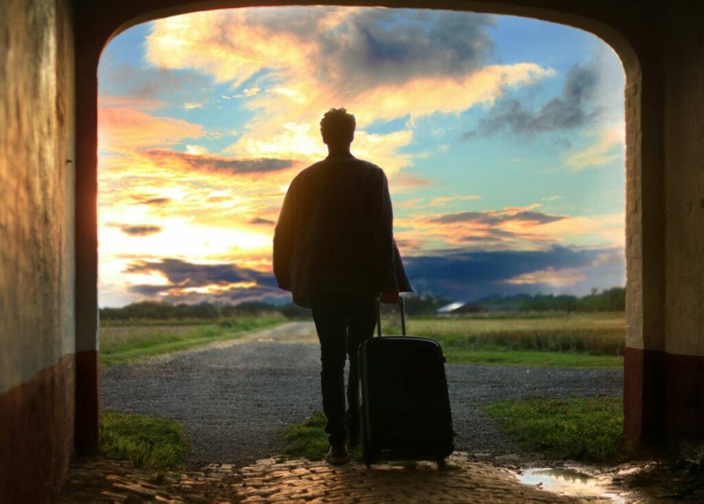 Back view of man with suitcase walking toward clouds