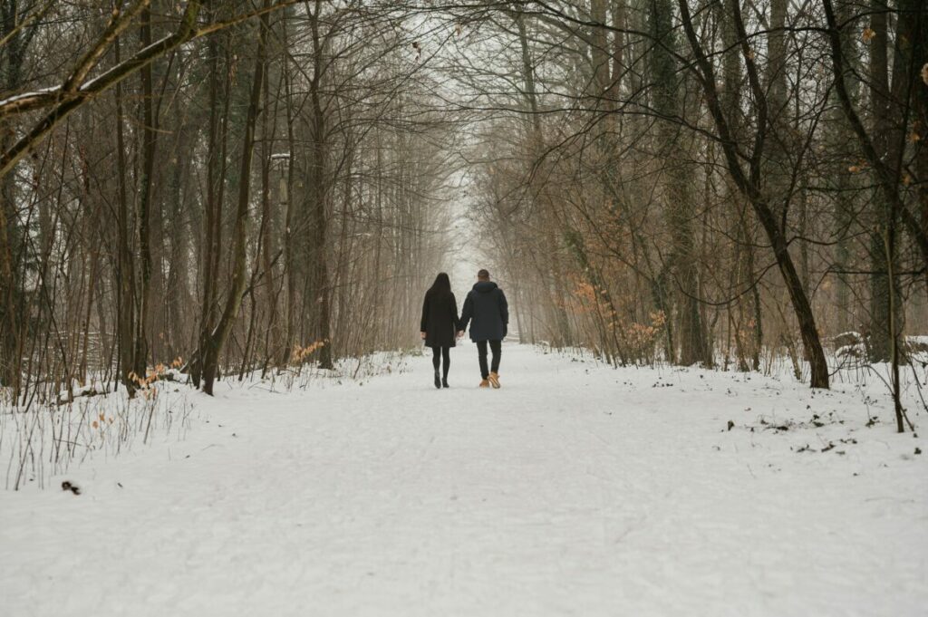 Photo of couple walking in snow under bare trees