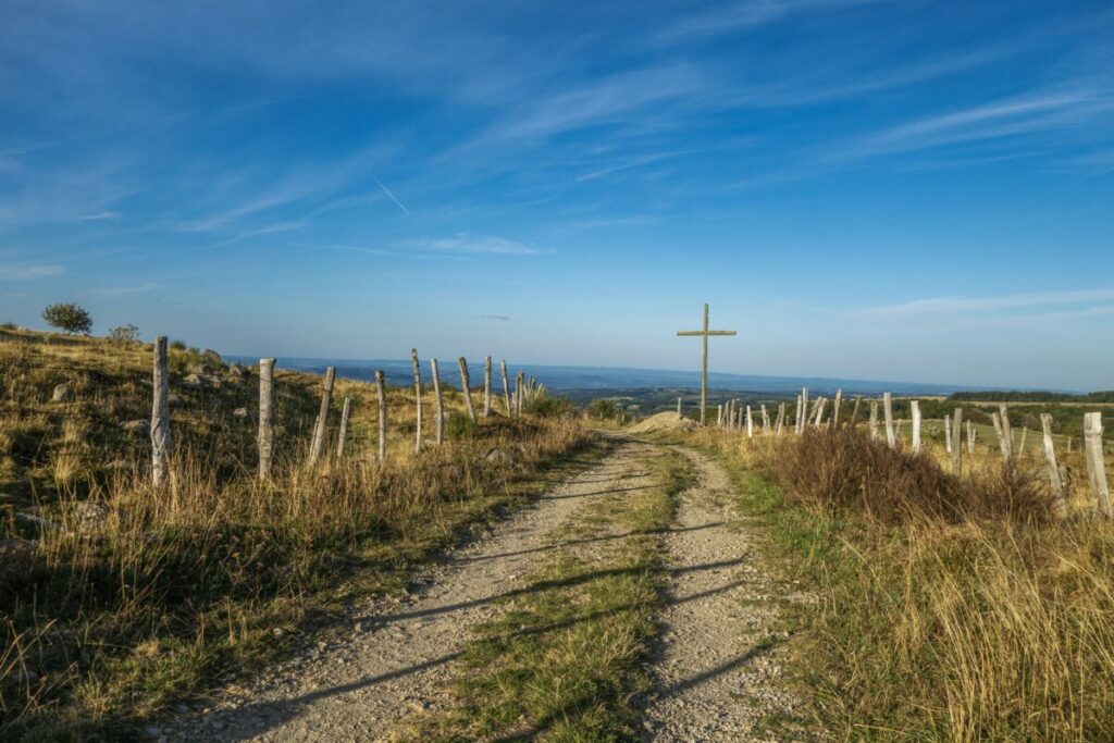 gravel road leading to wooden cross, blue sky