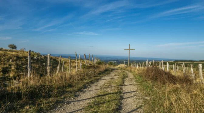 gravel road leading to wooden cross, blue sky