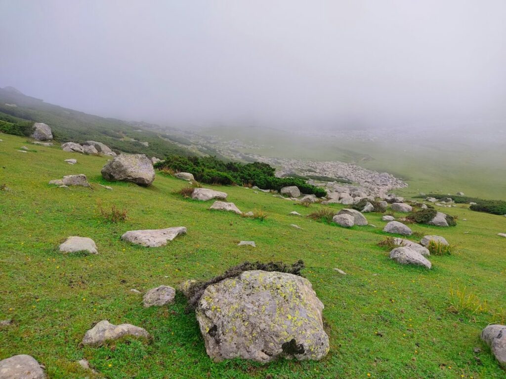 Photo of green hill with rocks, under fog