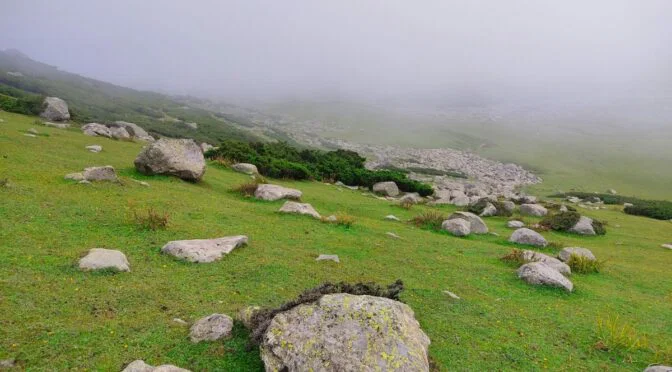 Photo of green hill with rocks, under fog