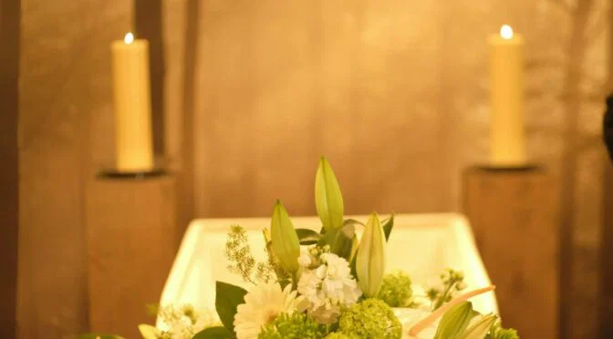 Photo of flowers in front of coffin with 2 candle on pillars on either side