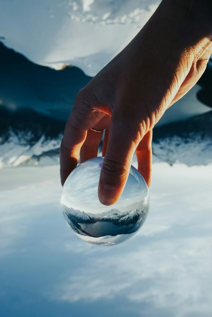Photo of a hand holding a glass orb with mountains in background